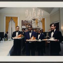 John H. Johnson and fellow butlers carry trays of "lobster en bellevue" from the Family Dining Room to the State Dining Room to serve them to guests at a State Dinner hosted by President Gerald R. Ford in honor of Emperor Hirohito of Japan on October 2, 1975. 